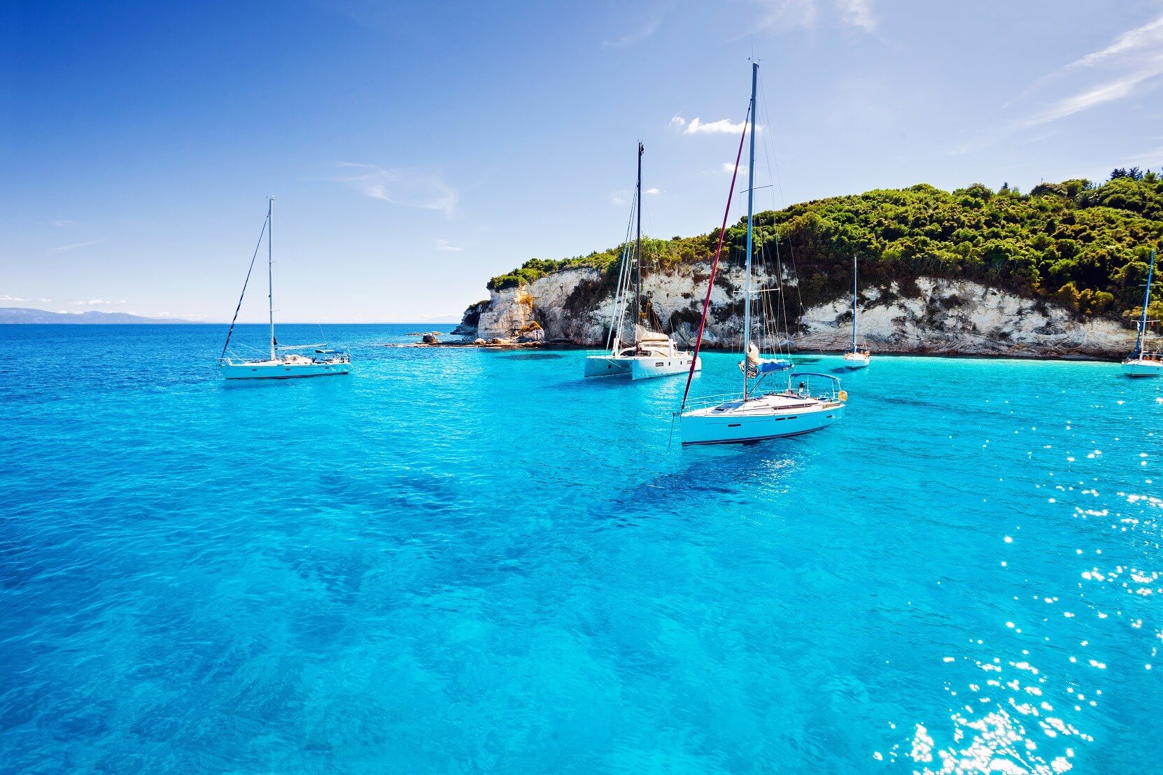 Turquoise and blue ocean with small green islands surrounded by white coasts and a speed boat sailing in the water